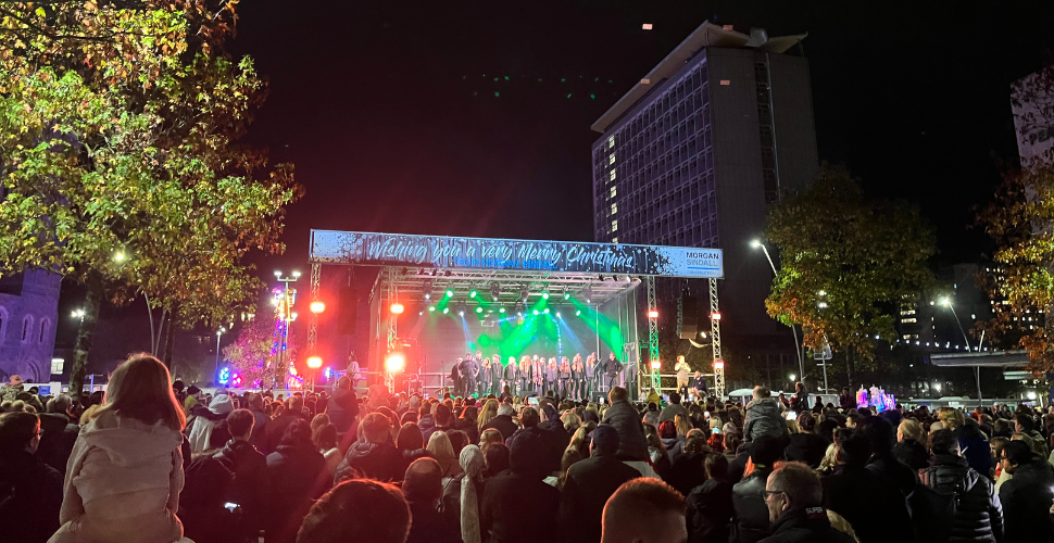 People looking at a stage with performers on there and a large building in the background